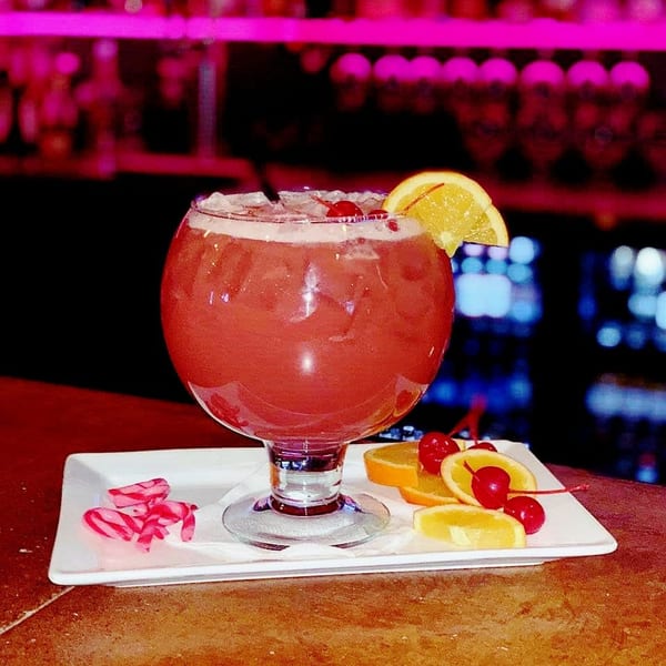 A large red cocktail with ice, an orange slice, and cherries on a white plate.