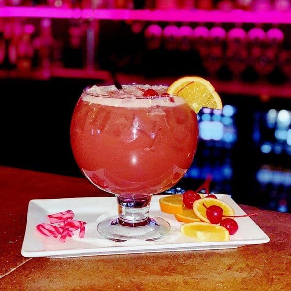 A large red Angelina's Mexican Restaurant cocktail with ice, orange slices, and cherries on a bar.
