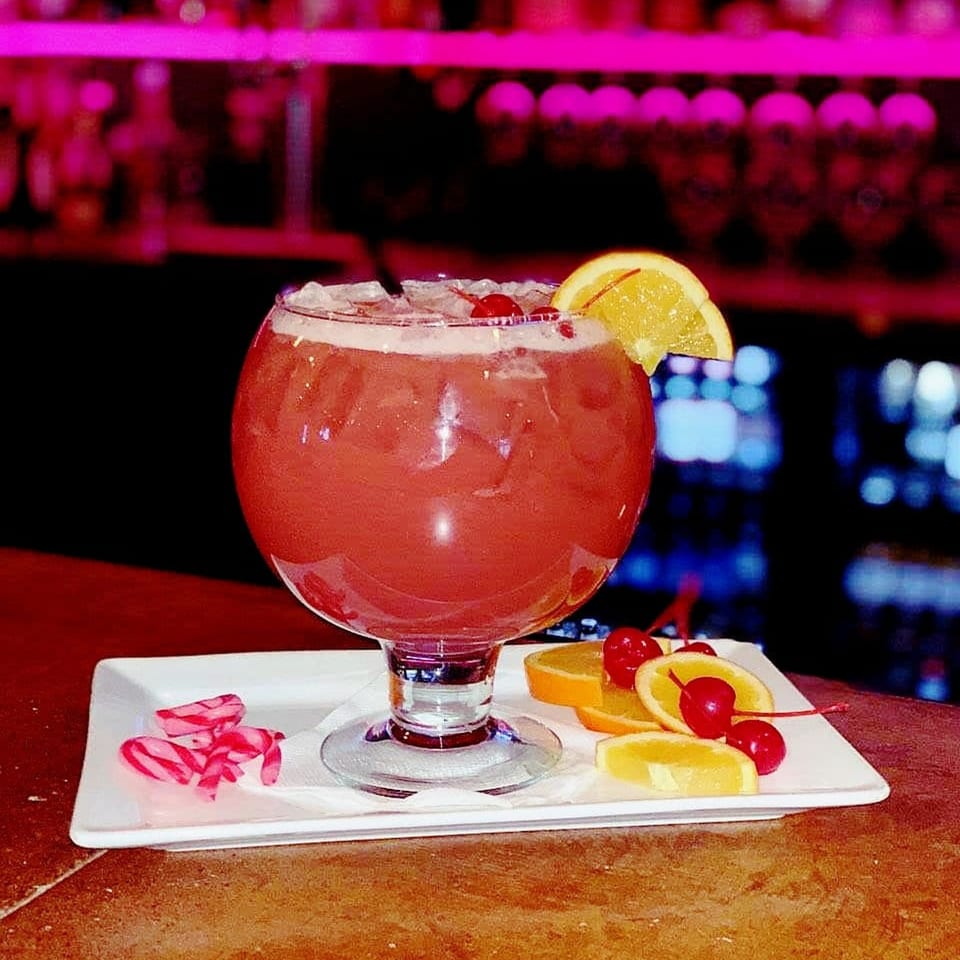 A large red Angelina's Mexican Restaurant cocktail with ice, orange slices, and cherries on a bar.