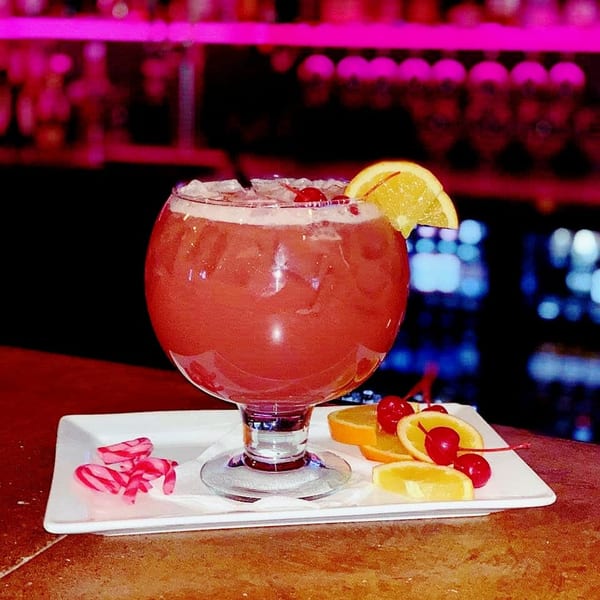 A large red cocktail with ice, an orange slice, and cherries on a white tray.