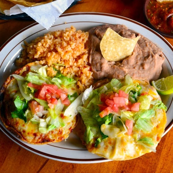 Two tostadas with melted cheese, lettuce, and tomatoes, served with rice and refried beans.