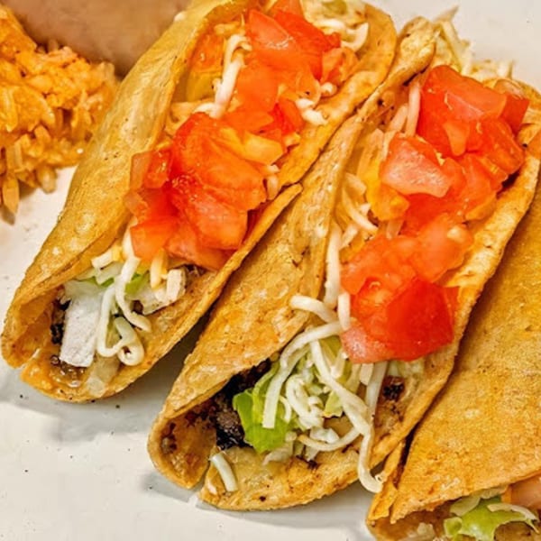 Three crispy Angelina's Mexican Restaurant tacos filled with meat, lettuce, cheese, and diced tomatoes.