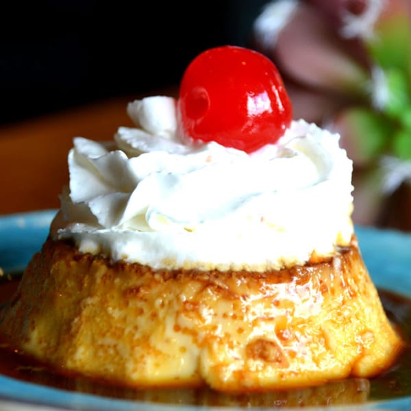 Angelina's Mexican Restaurant flan dessert with whipped cream and a cherry on a blue plate.