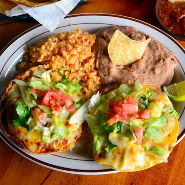Two cheesy tostadas topped with lettuce and tomatoes, served with rice, refried beans, and a lime.