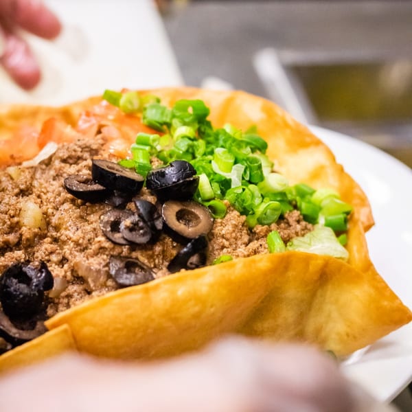 A taco salad in a crispy fried tortilla bowl, topped with ground beef, olives, and green onions.
