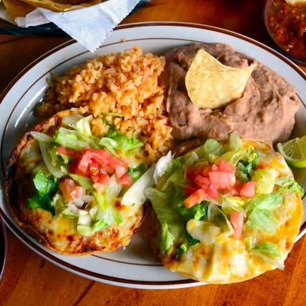 Two cheesy tostadas with lettuce and tomatoes, served with rice and refried beans.